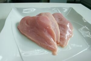 Pollo crudo su un tagliere, evidenziando il divieto di lavarlo prima della cottura.